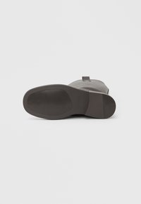 Καφέ δερμάτινη μπότα με λείο φινίρισμα, στρογγυλεμένη μύτη και υφασμένη λαστιχένια σόλα. Διαθέτει μικρό βοηθητικό ιμάντα στο τακούνι.