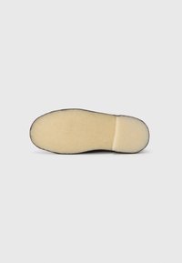 Suola di scarpa nera con un bordo in gomma texturizzato e una superficie interna liscia beige. Forma arrotondata con una sezione del tacco leggermente sollevata.