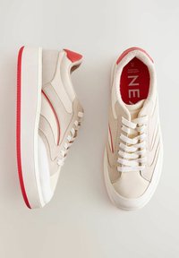 Sneaker in suede beige con dettagli rossi, presentano una punta liscia, lacci bianchi e un collare imbottito. La suola è bianca con il fondo rosso.