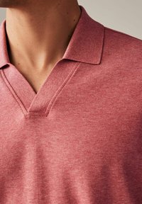 Rotes Polohemd mit strukturiertem Strick, ausgestattet mit einem V-Ausschnitt und einem klassischen Kragen. Steppdetails an den Kragenrändern sichtbar.