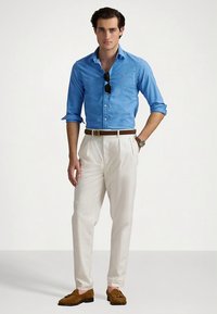 Ανοιχτό μπλε πουκάμισο με κουμπιά, λευκό πλισέ παντελόνι, καφέ ζώνη και μοκασίνια. Γυαλιά ηλίου στην κορυφή του πουκάμισου. Κλασική, εφαρμοστή γραμμή.