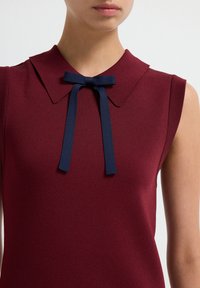 Abito senza maniche color bordeaux con colletto a punta e dettaglio in blu navy a fiocco al collo. Texture liscia, design aderente.
