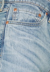 Vaqueros de mezclilla azul claro con un diseño clásico de cinco bolsillos, remaches de cobre y una textura sutil de arrugas.