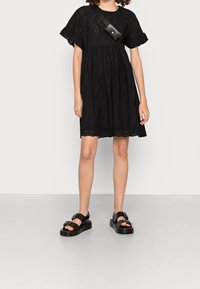 Vestido negro bordado con mangas cortas con volantes y una falda de capas. Combinado con sandalias de plataforma negras con un detalle de hebilla.
