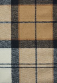Le tissu en tartan de laine présente un motif de carrés marron, beige, crème et noir, avec une texture douce et des détails de tissage visibles.
