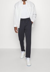 Ciemnoszare spodnie dresowe z elastycznym ściągaczem w pasie, w połączeniu z białym topem bez rękawów i koszulą w paski z guzikami, oraz białymi trampkami.