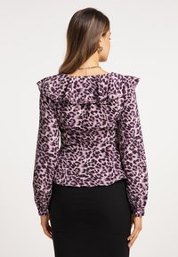 Violetti paita, jossa on röyhelökaulus ja pitkät hihat, ja joka esittää läikikäs leopardikuvio. Pehmeä kangas ja istuva malli.