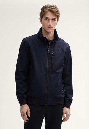 Marineblaues Jacket mit hohem Kragen, Reißverschluss und gerippten Bündchen. Verfügt über eine Brusttasche und eine glatte Textur. Eignet sich gut für die Freizeit.