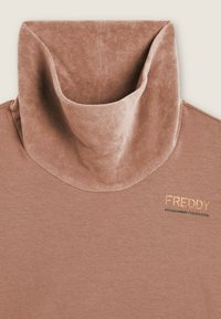 Top a maniche lunghe rosa polveroso con colletto alto e morbido. Presenta un tessuto testurizzato e "FREDDY" ricamato in oro con dettagli neri.