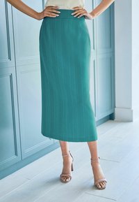 Teal, polvisen pituinen kynähame, jossa on pystysuora rakenne, korkea vyötärö ja suora leikkaus. Yhdistetty vaaleanpunaisiin nilkkaremmikenkiin.