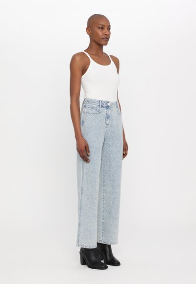 Hellblaue, hochgeschnittene Slim-Fit-Jeans mit leichtem Used-Look und fünf Taschen, kombiniert mit einem weißen Tanktop und schwarzen Stiefeletten mit Absatz.
