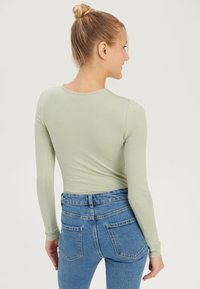 Long-sleeve, light green top paired with high-waisted blue jeans, featuring a classic denim texture and rear pockets.