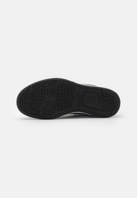Suola di sneaker in gomma nera con un motivo di presa testurizzato, caratterizzato da forme circolari e esagonali, e logo del marchio vicino all'area del tallone.