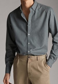 Camicia a maniche lunghe, con bottoni, di colore verde scuro con fantasia a quadri bianchi; tessuto morbido, bottoni a contrasto, design con colletto. Pantaloni beige.