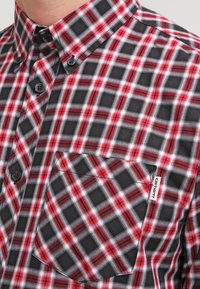 Mustapuna ruudullinen paita, jossa on napillinen kaulus. Paidassa on rintatasku ja pieni bränditarra taskussa. Materiaalina puuvilla.