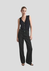 Blouse sans manches bleu marine avec un décolleté en V et cinq boutons, associée à un jean noir taille haute à large jambes et des sandales noires.