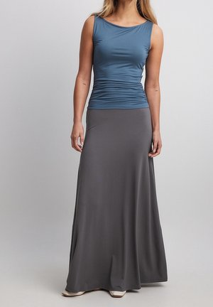 Haut bleu sans manches avec des détails froncés, associé à une longue jupe grise en tissu doux ; silhouette décontractée, sans motifs apparents.