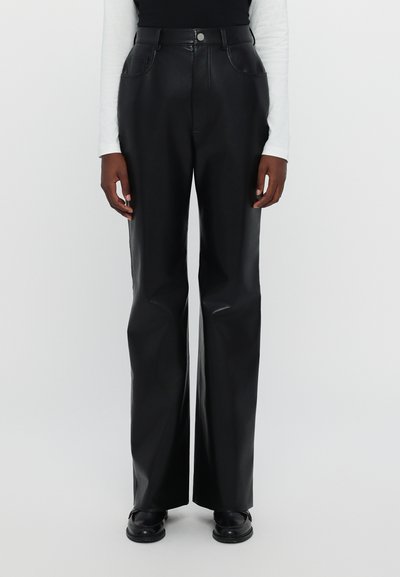 Pantalones de cuero negros de pierna ancha con una cintura alta, que cuentan con bolsillos delanteros y una textura suave y brillante. Combinados con calzado negro.