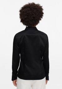Black long-sleeve shirt made of smooth fabric, featuring a tailored fit, buttoned cuffs, and a classic collar; minimalist design with no visible patterns.