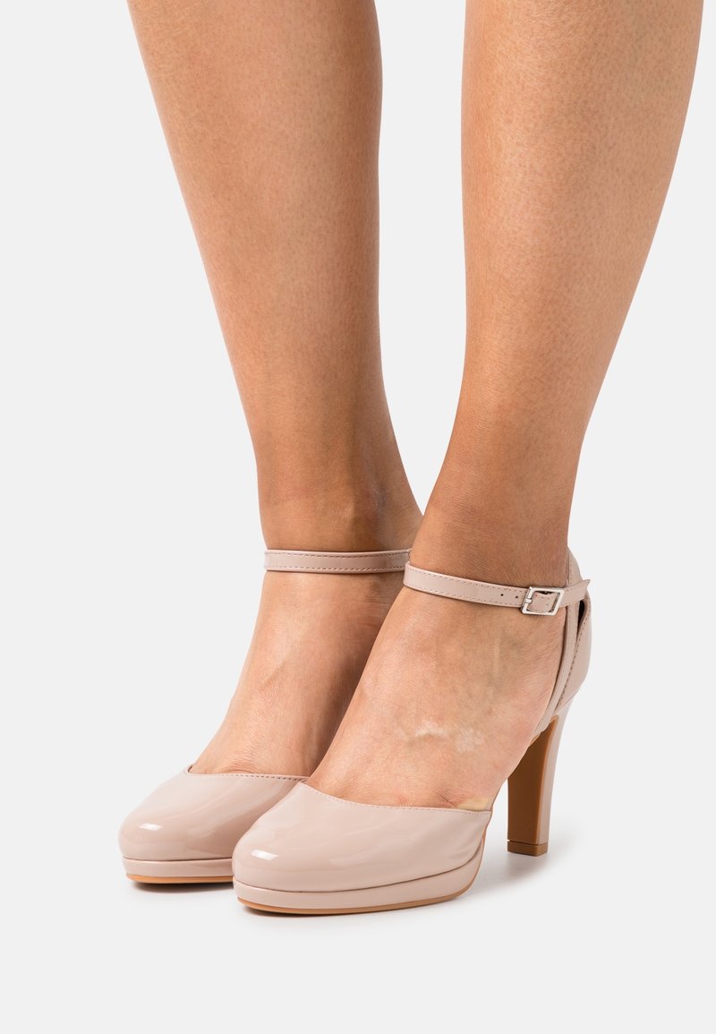 Escarpins en cuir verni beige avec un bout rond, une bride autour de la cheville et un talon bloc de 10 cm. Texture lisse et design minimaliste.