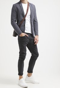 Grå strukturerad kavaj över en vit t-shirt, kombinerat med svarta uppvikta byxor och vita sneakers. Axelledväska med brun rem.