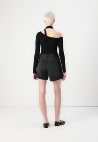 Zwarte lange mouw top met off-shoulder ontwerp, gecombineerd met high-waisted grijze denim shorts, weergegeven vanaf de achterkant.