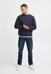 Marineblå genser med rund hals og "blend"-logo; kombinert med mørke jeans og hvite joggesko; glatt stoff, avslappet passform.