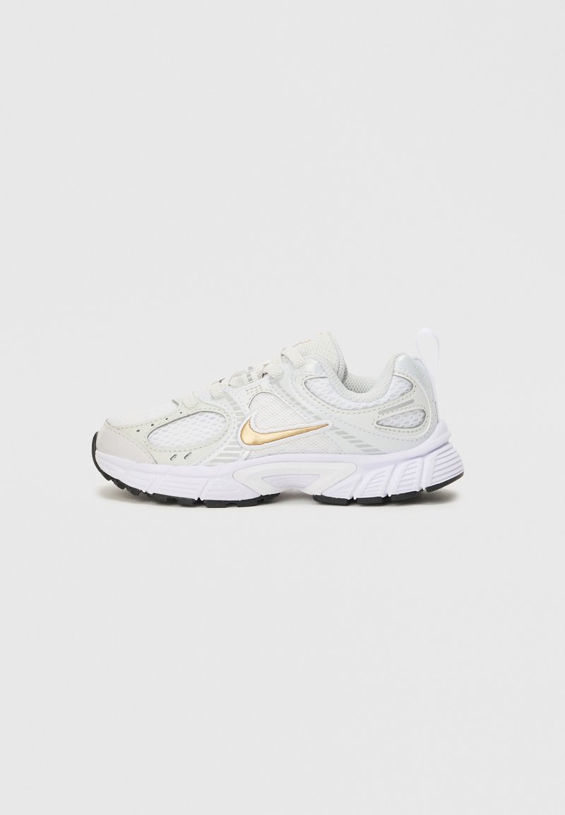 Zapatilla deportiva blanca con parte superior de malla transpirable, acentos dorados, suela texturizada y punta redonda. Presenta cordones y una tira para tirar en el talón.