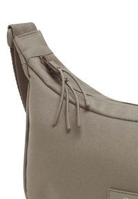 Borsa a spalla in tessuto marrone con una superficie liscia, chiusura con cerniera e due cordini. Presenta una patch rettangolare con logo sulla parte anteriore.