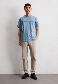 Lichtblauwe katoenen t-shirt met het logo "Marc O'Polo", gecombineerd met beige broeken en zwarte veterschoenen. Eenvoudig ontwerp, klassieke pasvorm.
