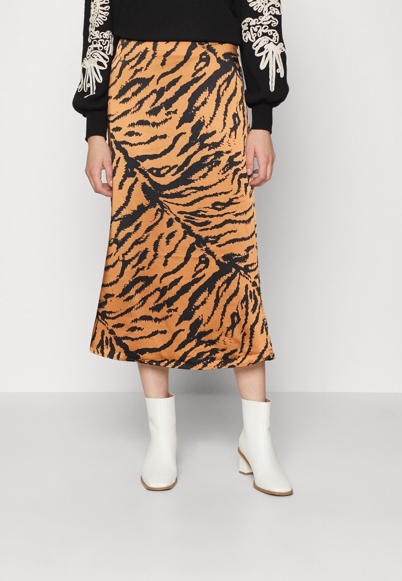 Jupe à imprimé tigre orange en tissu lisse, tombant à mi-mollet, accompagnée de bottines blanches à talon bloc.