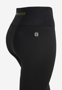 Mustat legginssit, jotka on valmistettu joustavasta materiaalista, jossa on leveä vyötärönauha ja huomaamaton hopeinen logotyyli alavatsassa.