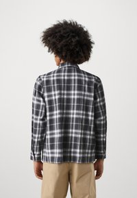 Black and white plaid shirt with long sleeves, a classic collar, and buttoned cuffs. Soft fabric; back view shows even plaid pattern.