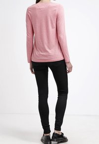 Rosa långärmad topp i ett lättviktigt tyg, i kombination med svarta skinny jeans. Toppen har en rundad halsringning och rak skärning.