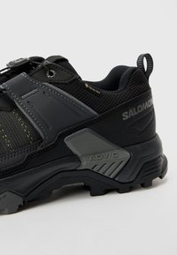 Svart utomhussko med överdel i mesh, plastöverdrag och strukturerad sula. Utrustad med ett snabb-snörningssystem och "GORE-TEX"-logotyp.
