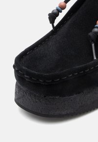 Sapato de camurça preto com sola de plataforma grossa, detalhes cosidos e contas decorativas nos atacadores para adicionar um toque especial.