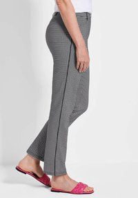 Schwarz-weiß karierte Hose mit tailliertem Design und seitlicher Nahtdetails. Kombiniert mit rosa gewebten Sandalen, was einen lässigen Look ergibt.