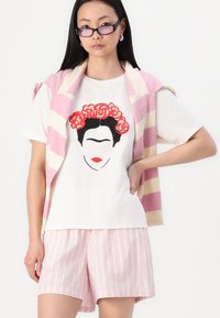 Grafisk T-skjorte med Frida Kahlo kunst, kombinert med en rosa og kremstripete cardigan drapert over skuldrene og lyserosa stripete shorts.