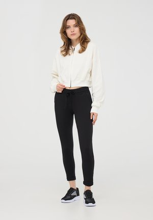 Felpa bianca corta con maniche lunghe, pantaloni sportivi neri slim-fit con cintura elastica e scarpe da ginnastica nere con suole bianche.