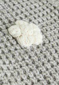 Tissu tricoté gris avec un tissage dense et une surface texturée, présentant un motif de fleur duveteuse bien visible en blanc cassé.