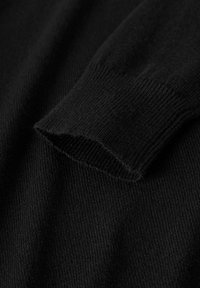 Tissu de pull noir avec une finition côtelée au poignet et une texture lisse, présentant un bord légèrement effiloché à l'ouverture des manches.