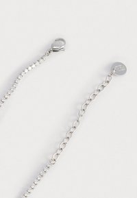 Collana in argento con una fila di strass trasparenti e un gancio a granchio. Include un ciondolo circolare con dettagli del logo.