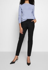 Ljuslila stickad tröja med långa ärmar, kombinerad med svarta slim-fit byxor. Svarta spetsiga klackskor fulländar outfiten.