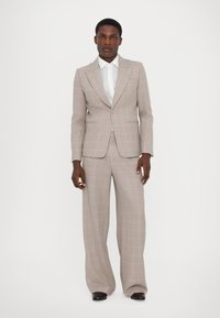 Completo a righe grigio chiaro con giacca monopetto e pantaloni a gamba larga. Presenta un motivo a quadri rosa e una camicia bianca classica sotto.