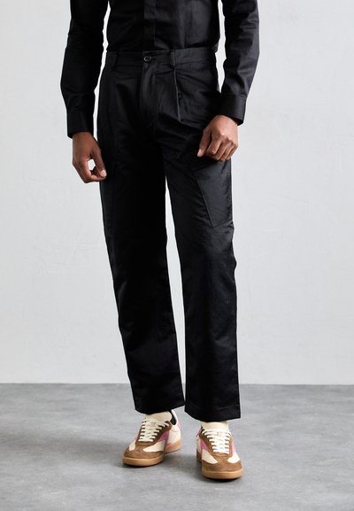 Pantalon noir à coupe droite, avec des poches latérales. Assorti à des baskets beige, rose et blanches avec des lacets et des accents texturés.