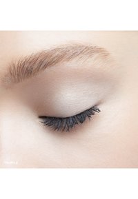 Nahaufnahme eines Auges mit einem glatten, hellbeigen Augenlid, langen, dunklen Wimpern und einer natürlichen, gepflegten Augenbraue in sanften, gedämpften Farbtönen.