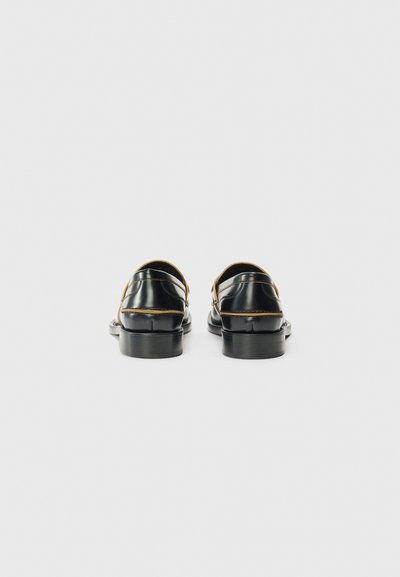 Chaussures noires avec des accents marron et un petit talon, présentées de l'arrière sur un fond blanc uni.