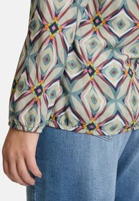 Multicolored patterned blouse featuring a geometric design with blue, pink, and yellow accents. Elasticized cuffs; lightweight fabric.