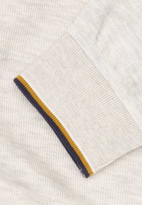 Crème kleurige trui-manchetten met ribbelstructuur, voorzien van marineblauwe en mosterdgele gestreepte accenten langs de rand. Zachte stof met een subtiel patroon.