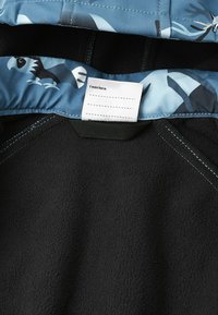 Zwarte fleecejas met een blauw patroon aan de binnenkant met vogels. Bevat een label met "Ik was hier:" en een ophanglus bij de hals.